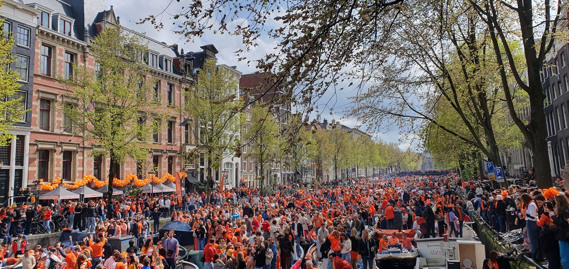 Grupo de personas vestidas de naranja celebrando el Día del Rey en las calles de Ámsterdam, una festividad llena de alegría y tradición.